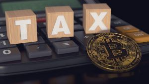 Bitcoin against calculator and wooden blocks with TAX letters on it. Taxes on bitcoin investments concept.