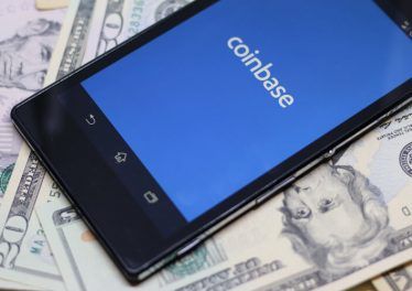 Coinbase android app on dollar background. Coinbase is a digital currency exchange.
