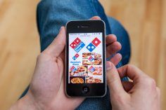 male hand holding iPhone with Domino's pizza delivery images in Google search on the display.