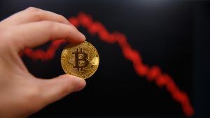 Man holding a Bitcoin with falling price chart in the background. 