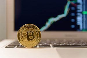Bitcoin on a laptop with rising price chart in the background. 